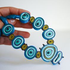 a hand holding a beaded bracelet made out of blue and gold beads on a white background