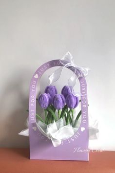 purple tulips in a paper bag with white ribbon on the front and bottom