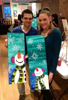 a man and woman holding up two snowman paintings