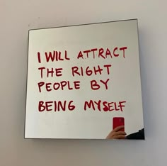 a person holding a cell phone in front of a white board with writing on it that says, i will attract the right people by being my self