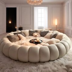 a large circular couch with pillows on top of it in front of a chandelier