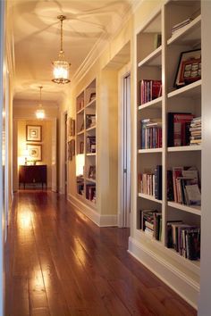 an empty hallway with bookshelves and lamps on either side of the room,