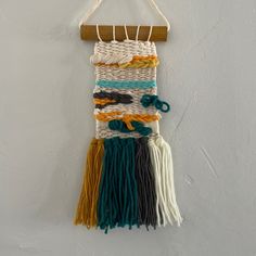 a wall hanging made out of different colored yarns and wood pegs on a white wall