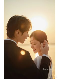 a man and woman standing next to each other in front of the ocean at sunset