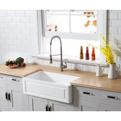 a white kitchen sink sitting under a window next to a counter top with fruit and vegetables on it