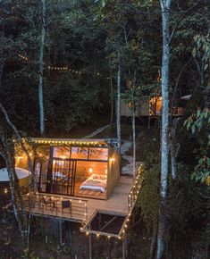 a small cabin nestled in the woods with lights strung from it's roof and deck