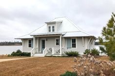 a white house sitting on top of a grass covered field next to a body of water