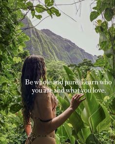 a woman is standing in the jungle with her back to the camera and looking at trees