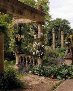 an outdoor garden with lots of plants and flowers on the sides of it, along with stone pillars