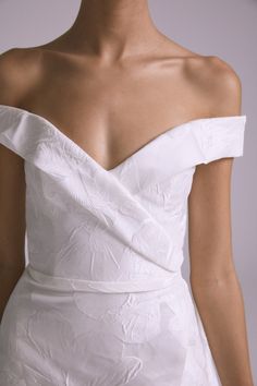 a woman wearing a white wedding dress with an off the shoulder neckline