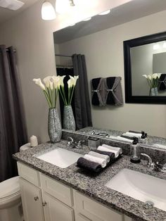 a bathroom with two sinks, mirrors and flowers in vases on the counter top