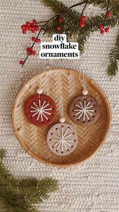 two wooden ornaments are hanging on a wicker tray next to pine branches and red berries