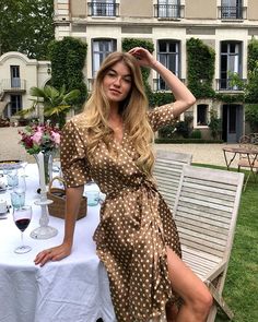 a woman sitting at a table with a wine glass in her hand and wearing a polka dot dress