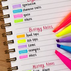 a notebook with some writing on it and several colored markers next to it, all lined up in different colors