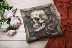 a decorative pillow with a skull and roses on it next to some flowers in the background