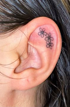 a woman's ear has a small flower tattoo on it