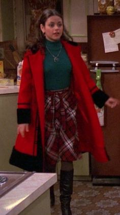 a woman in a red coat and plaid skirt standing next to a stove top oven