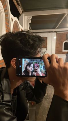 a man taking a photo with his cell phone while wearing a leather jacket and black shirt