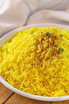 a white bowl filled with yellow rice on top of a wooden table