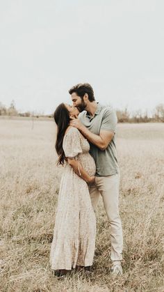 a pregnant couple kissing in a field