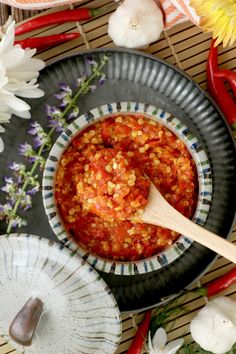 a bowl filled with chili sauce next to paper plates and flowers on a table top