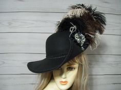 Ladies Black Cavalier woolen hat with black braided trim, black, brown and beige ostrich feathers on the left side of the hat, black cocarde with a sparkly jewel center. The turnup on the side is about 4" Please measure your head, I CANNOT make this hat larger.This hat is 22.5" for the inside circumference but does have a built-in hat sizer.  Please let me know if you have any questions All sales are FINAL, no returns or exchanges please keep this in mind before purchasing. International buyers: Please know that you will be held responsible for any CUSTOMS FEES. Please check with you local post office, before ordering to see what the customs fee rate is before you purchase Adjustable Black Boater Hat With Flat Crown, Black Pirate Costume Hat With Curved Brim, Musketeer Hat, Black Steampunk Brimmed Hat, Black Adjustable Pirate Hat, Cavalier Hat, Vintage Black Hat With Feathers, Woolen Hat, Pirate Hat