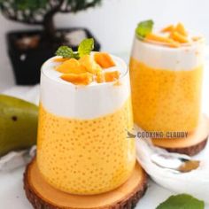 two glasses filled with food sitting on top of a wooden slice next to a plant