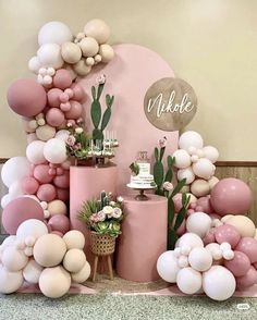 a table topped with balloons and cake next to a wall covered in pink, white and gold balloons