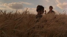 two people standing in tall grass under a cloudy blue sky