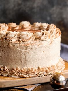 a close up of a cake with frosting on a wooden platter next to a serving utensil