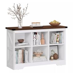 a white bookcase with books and vases on top of it next to a bowl of fruit