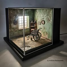 an old wheelchair in a glass case on the floor and inside is a room with green walls