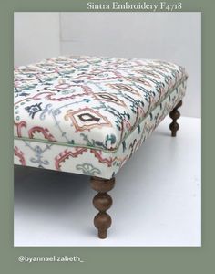 an upholstered footstool with wooden legs and colorful fabric on the top