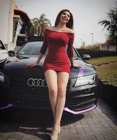 a woman in a red dress standing next to a black car