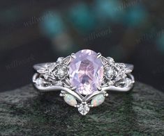 a ring with an oval pink stone surrounded by white diamonds on top of a rock