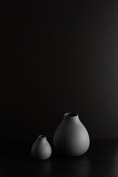 two white vases sitting on top of a wooden table in front of a black wall