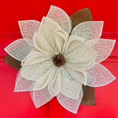 a large white flower with green leaves on a red front door, decorated with burlap