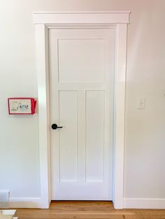 an empty room with a white door and wooden floor in front of the door is a clock on the wall