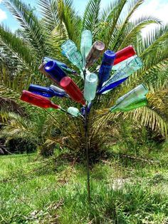 a tree made out of glass bottles sitting on top of a lush green field next to a palm tree