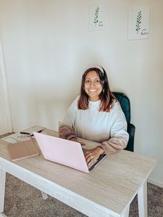 a woman sitting at a desk with a laptop computer on her lap and smiling for the camera