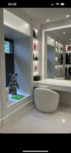 a teddy bear sitting on a stool in front of a large mirror and shelves with clothes