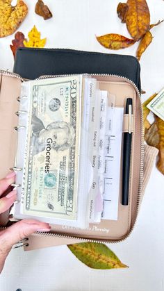 a woman holding a wallet filled with money and cash notes in front of fall leaves