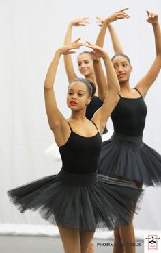 three ballerinas in black tutu and leotards with their hands up