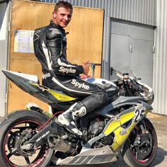 a man sitting on top of a yellow and black motorcycle in front of a building