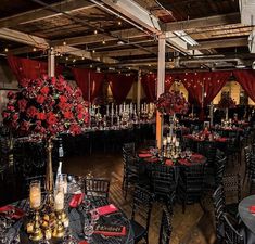 a room filled with tables and chairs covered in black linens, red flowers and candles