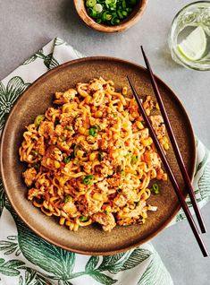 a brown plate topped with noodles and chopsticks next to a glass of water