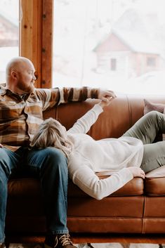 a man and woman sitting on top of a brown leather couch next to each other