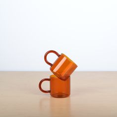 two orange coffee mugs sitting on top of a wooden table next to each other