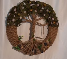 a rope wreath with a tree on top and flowers around the edges, hanging from a hook