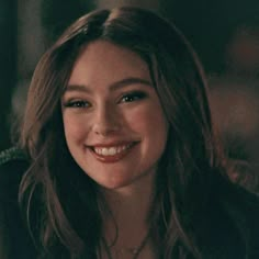 a close up of a person wearing a necklace and smiling at the camera with a smile on her face